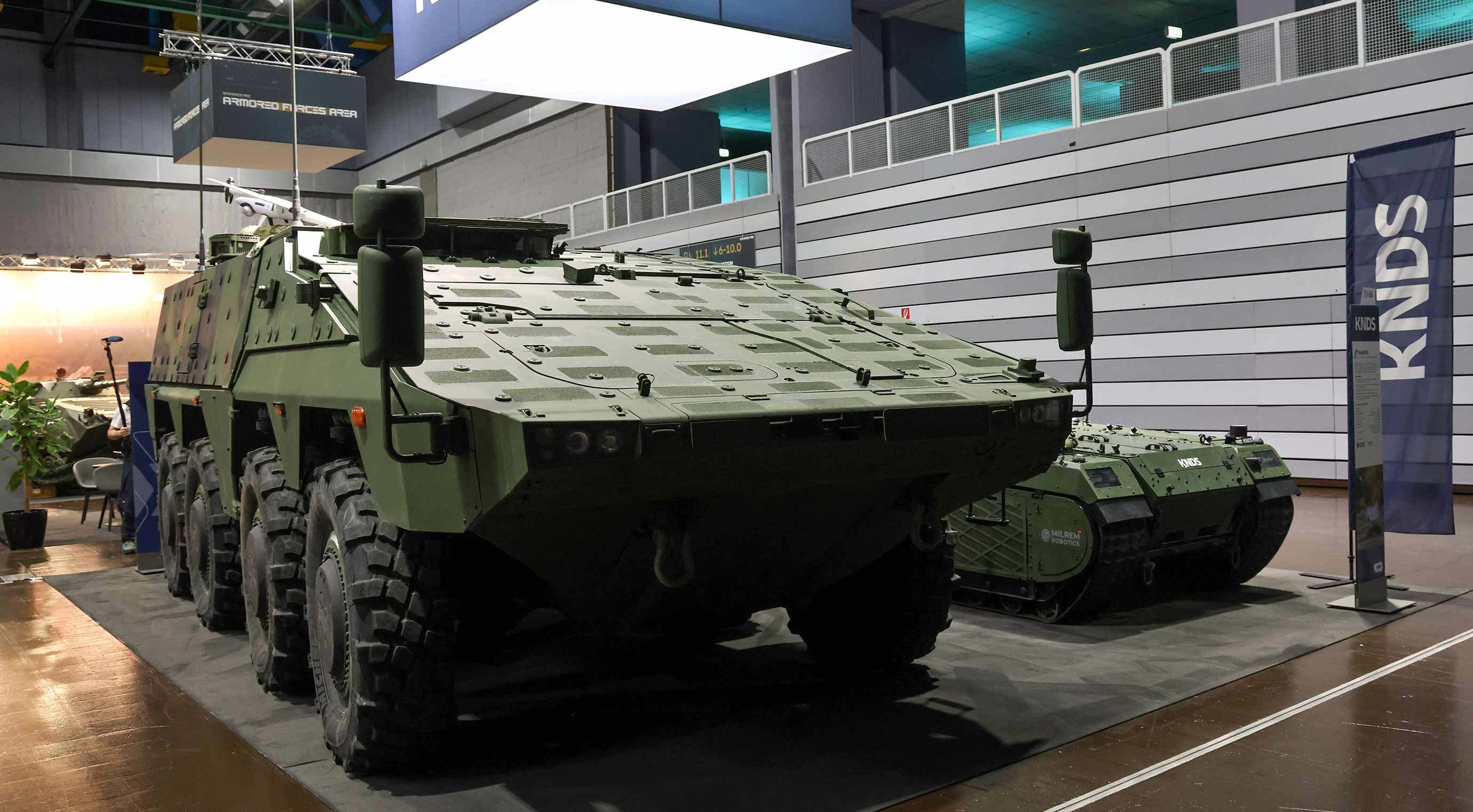 Armoured multi-purpose vehicle and unmanned robot at the exhibition stand; military vehicles in the exhibition hall.