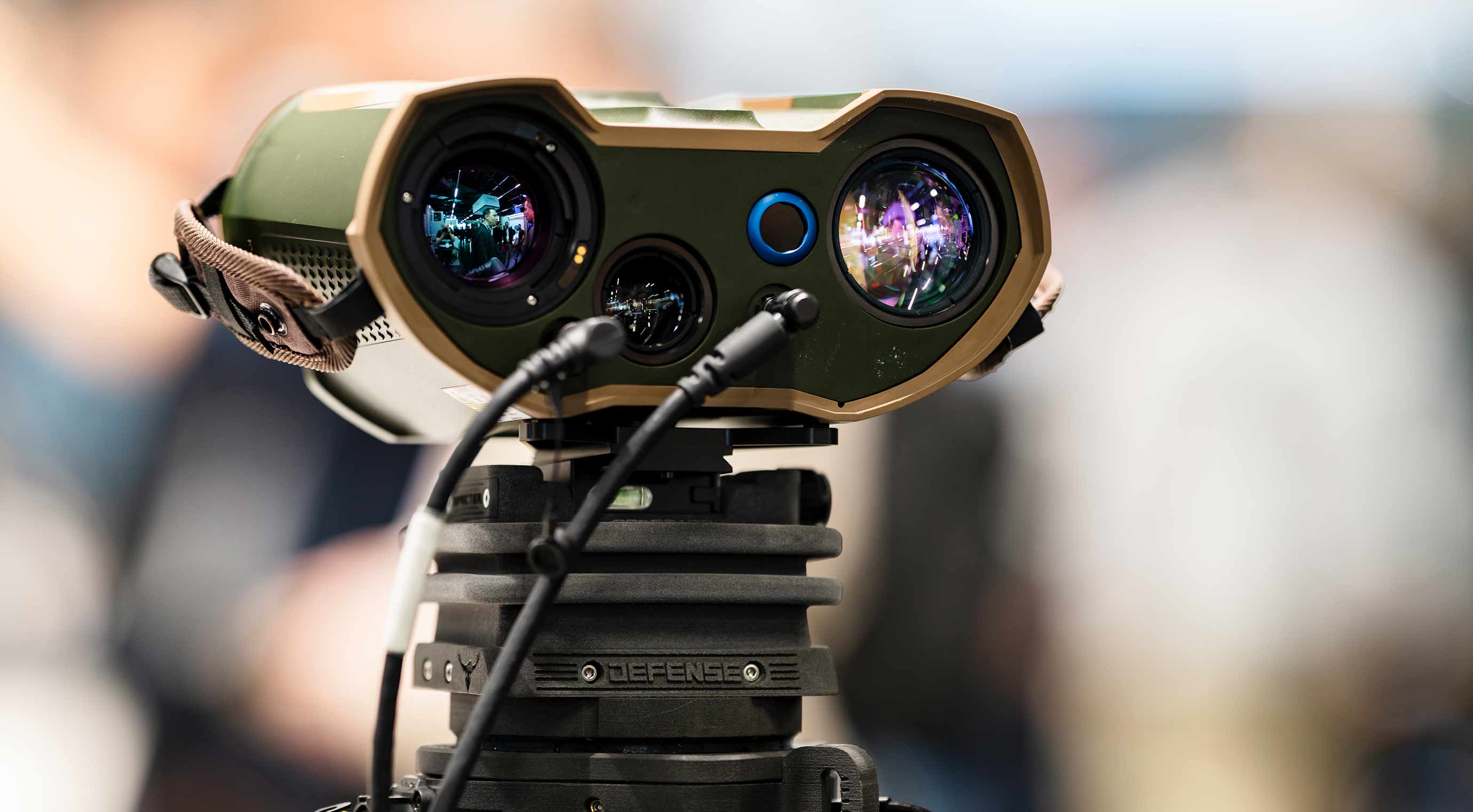 Close-up of an optical sensor on a tripod, with lenses and cables, displayed at a trade show.
