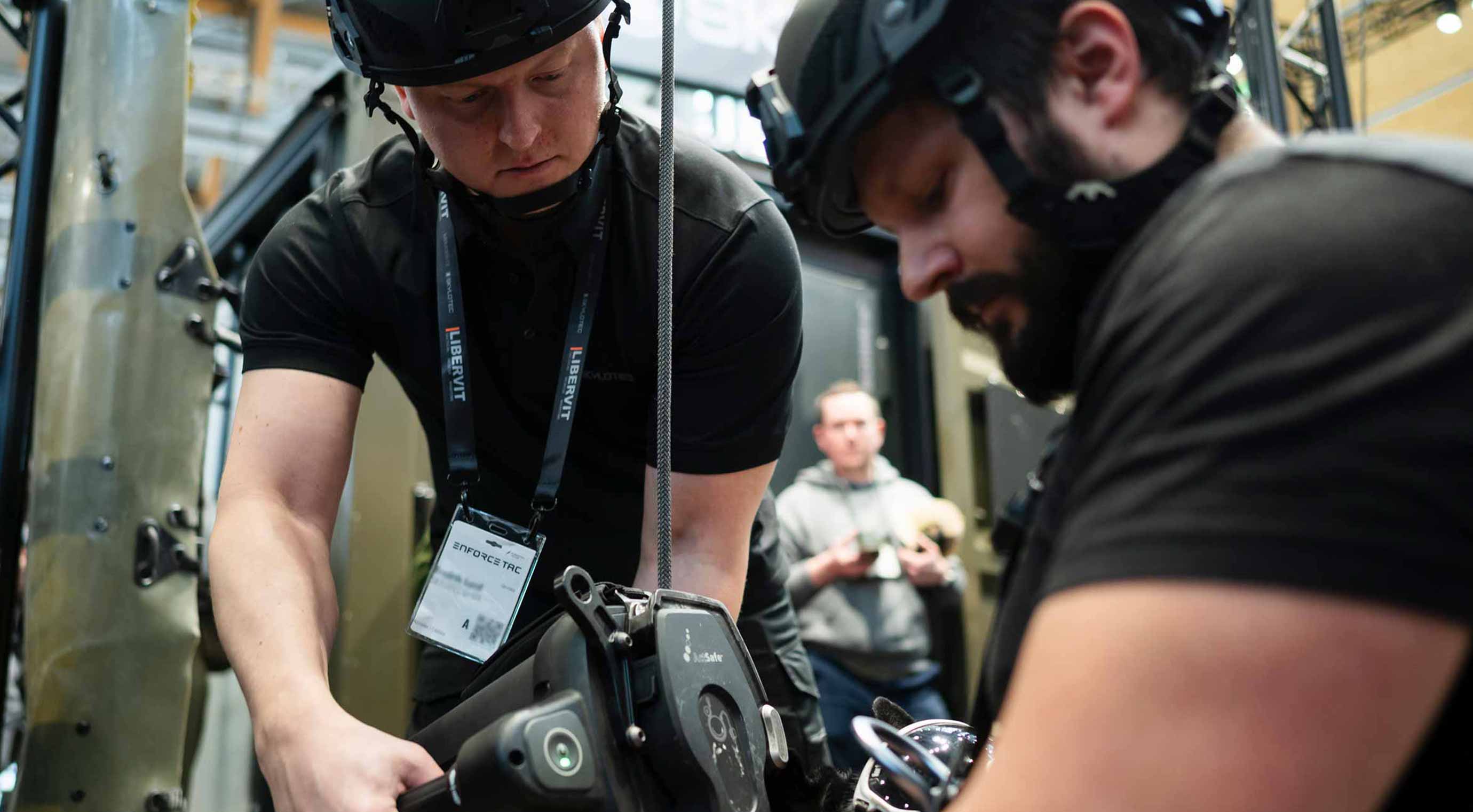 Practical exercise at the exhibition stand: People wearing helmets test a rappelling device in the exhibition hall.